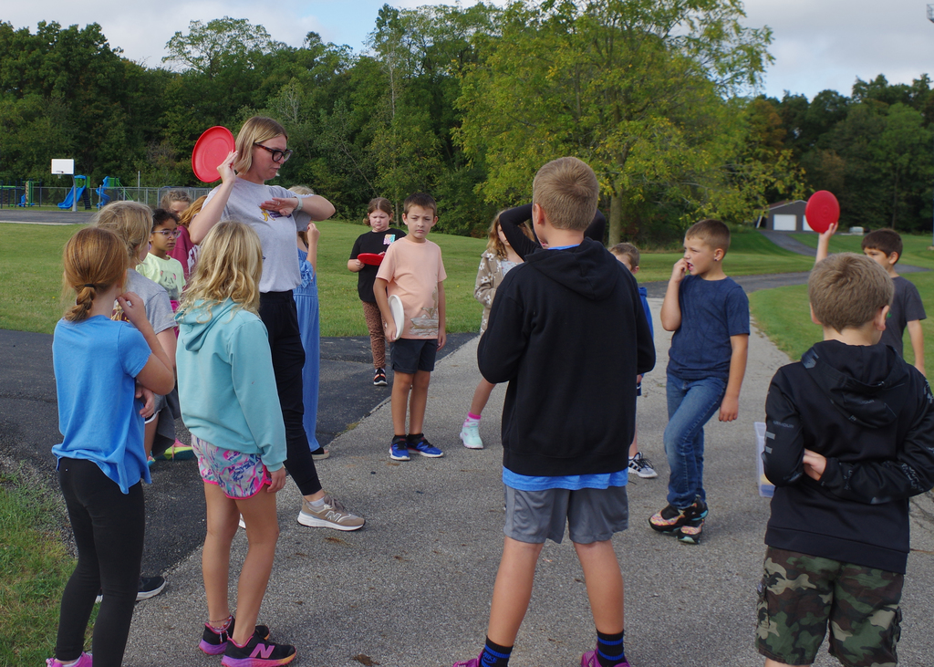 teacher showing group of students how to throw a frisbee