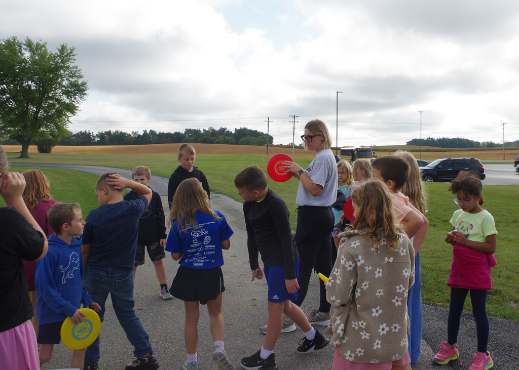 teacher showing group of students how to throw a frisbee