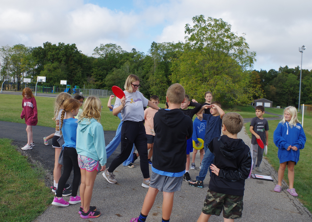 teacher showing group of students how to throw a frisbee