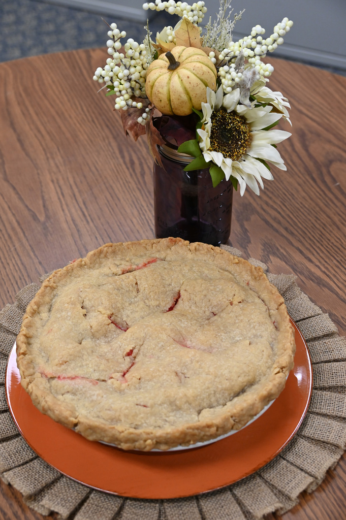 pie sitting on table with flowers behind it