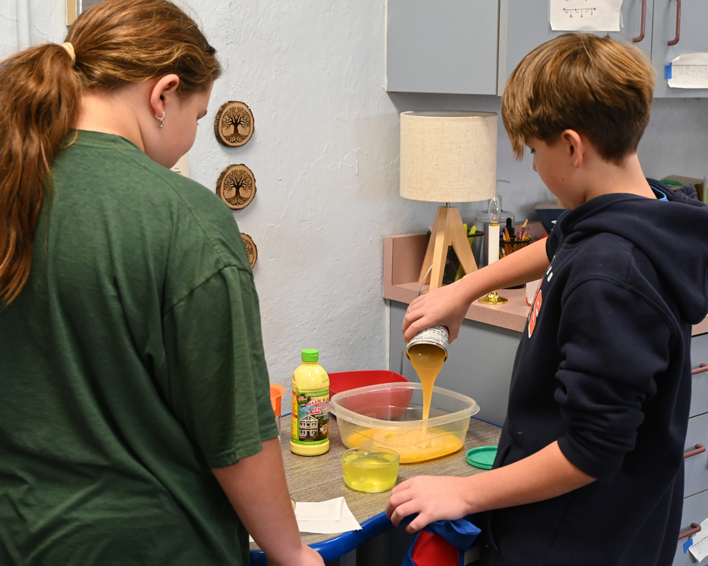 two kids pouring ingredients into a dish