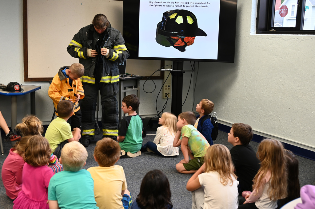 class of children watching child and adult put on fire gear