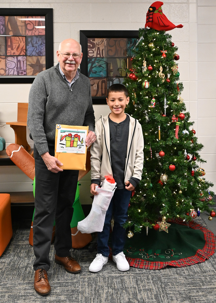 man holding envelope and boy holding christmas stocking standing in front of tree