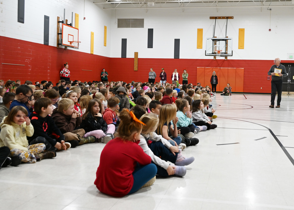 lots of childern sitting in gym looking at man talking in front