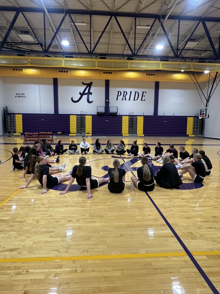 Girls basketball team sitting in circle on gym floor