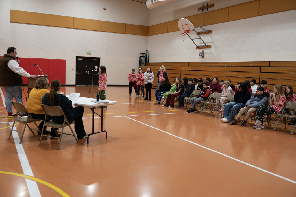 students in row of chairs in front os 3 adults 