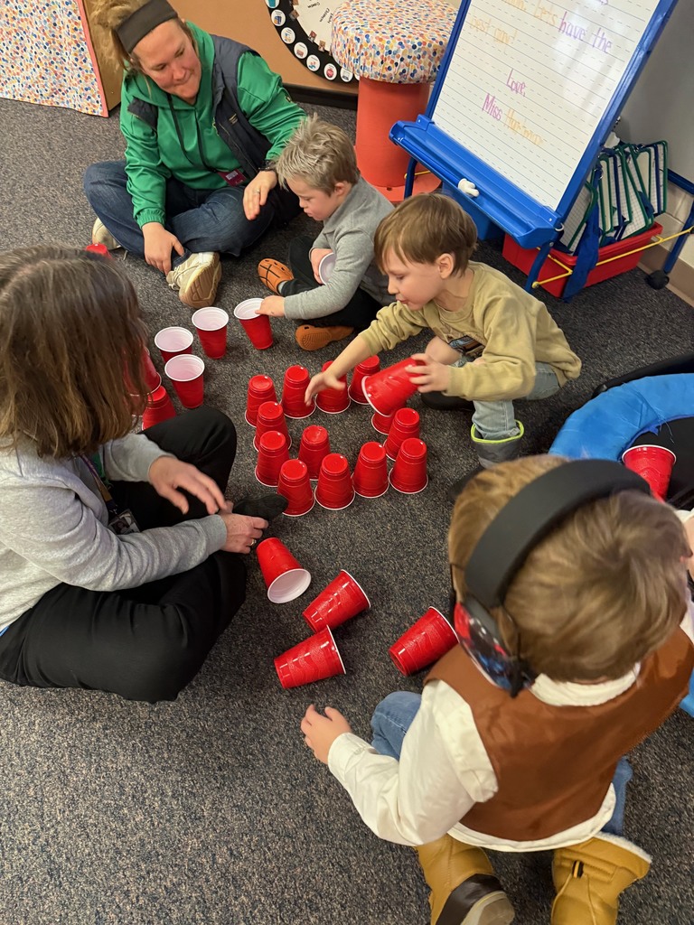 4 children and 1 adult playing with red cups on the floor