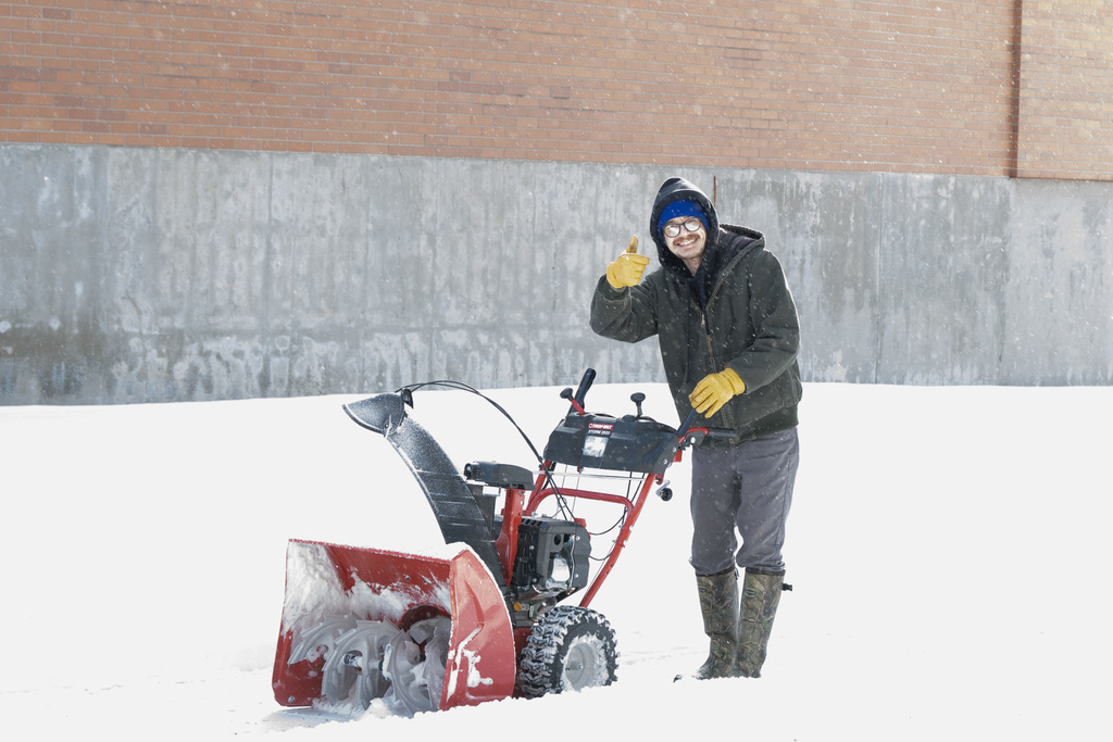 man giving thumbs up as he snow blows a sidewalk