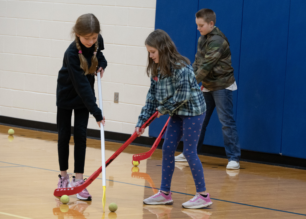 three elementary students practicing hockey with sticks and balls