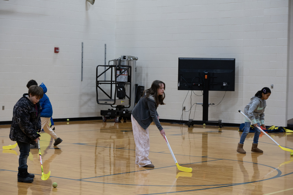 3 elementary students practicing hockey with sticks and ball