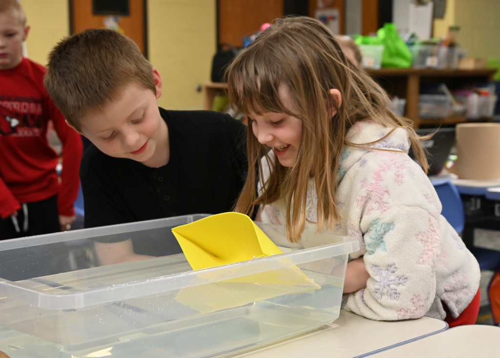 two childern looking in a conatain of water floating a hand made boat