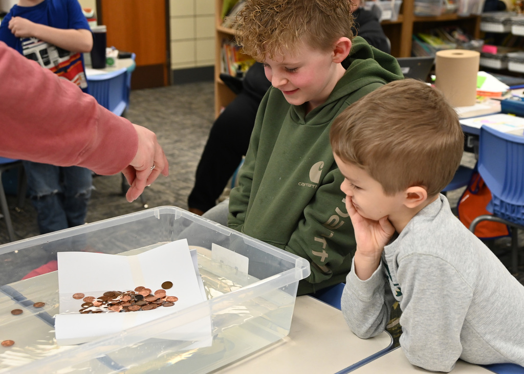 two childern looking in a conatain of water floating a hand made boat