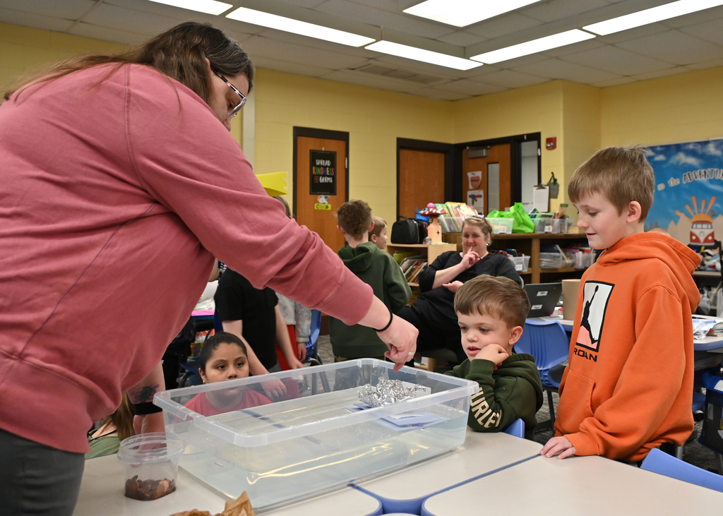 two childern looking in a conatain of water floating a hand made boat