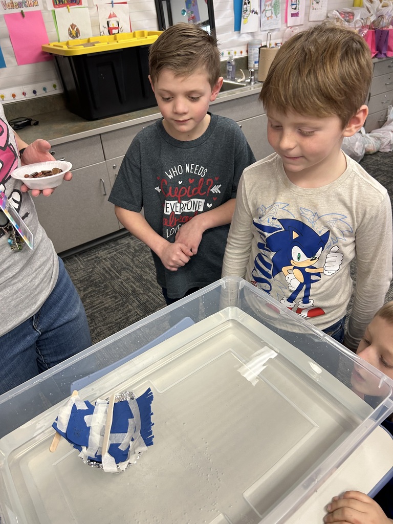 two childern looking in a conatain of water floating a hand made boat
