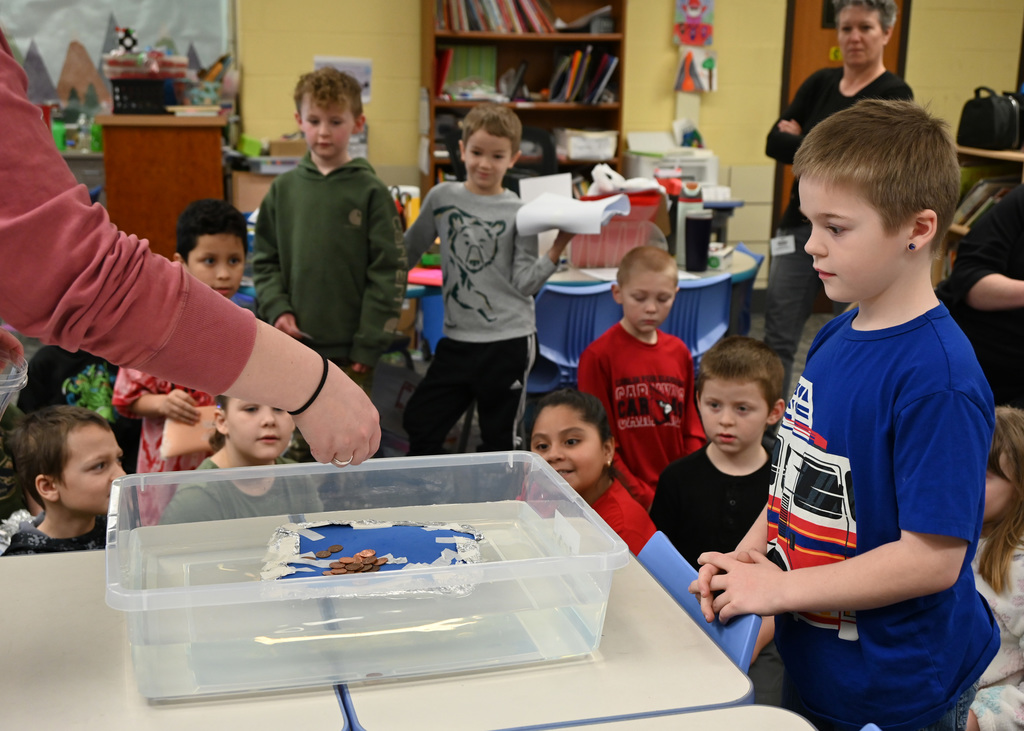 student looking in a conatain of water floating a hand made boat that is getting pennies added to it
