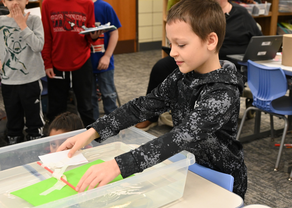 child looking in a conatain of water floating a hand made boat