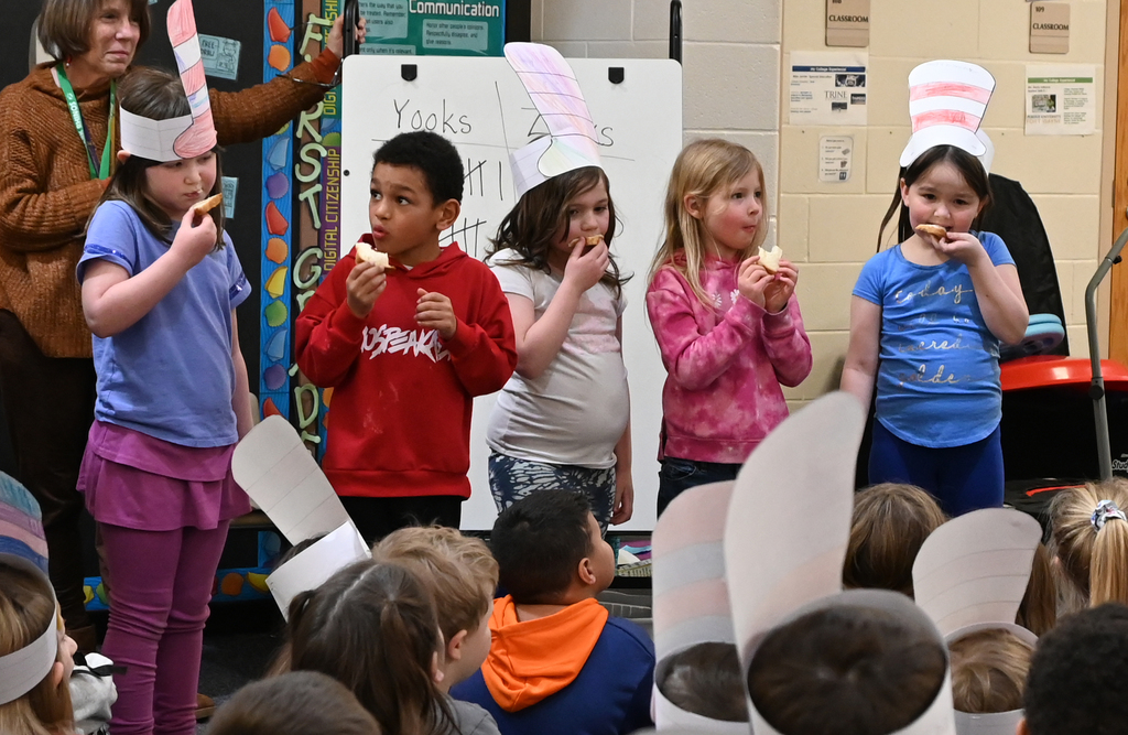 5 students taking a bite of bread in front of class