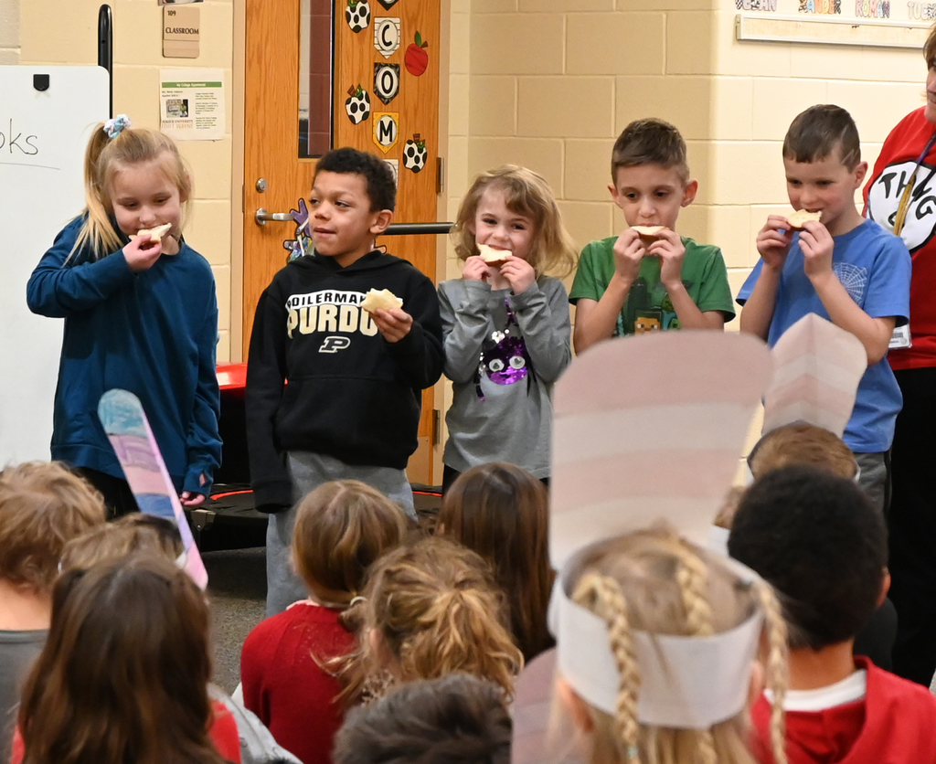 5 students taking a bite of bread in front of class