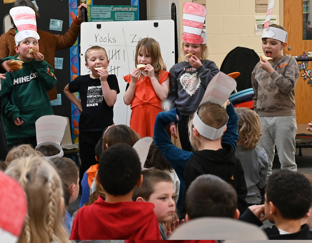 5 students taking a bite of bread in front of class