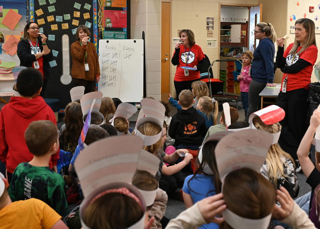 Teachers standing in front of students taking a bite of bread