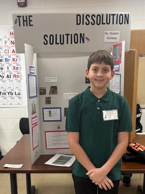 boy standing in front of poster display for science fair