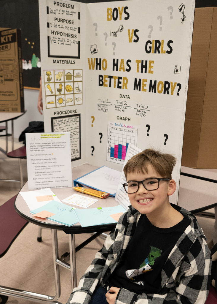 boy sitting in front of poster display for science fair