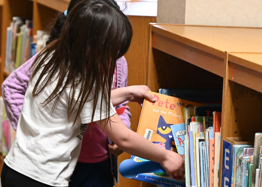 two children pulling a book of a shelf
