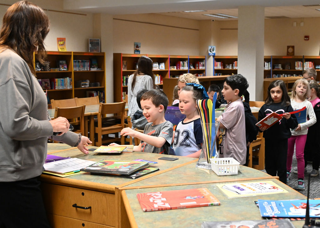 childern in line at a library handing book to librarian