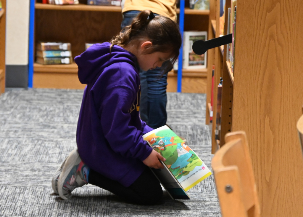 child sitting on floor in front of bookshelf looking at a book
