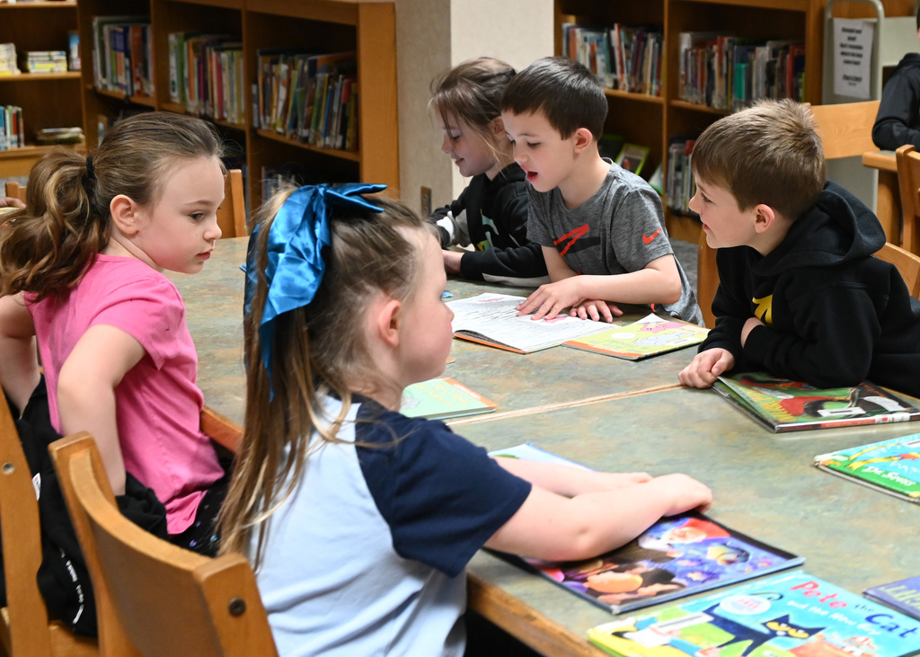 five children sitting around a table reading books