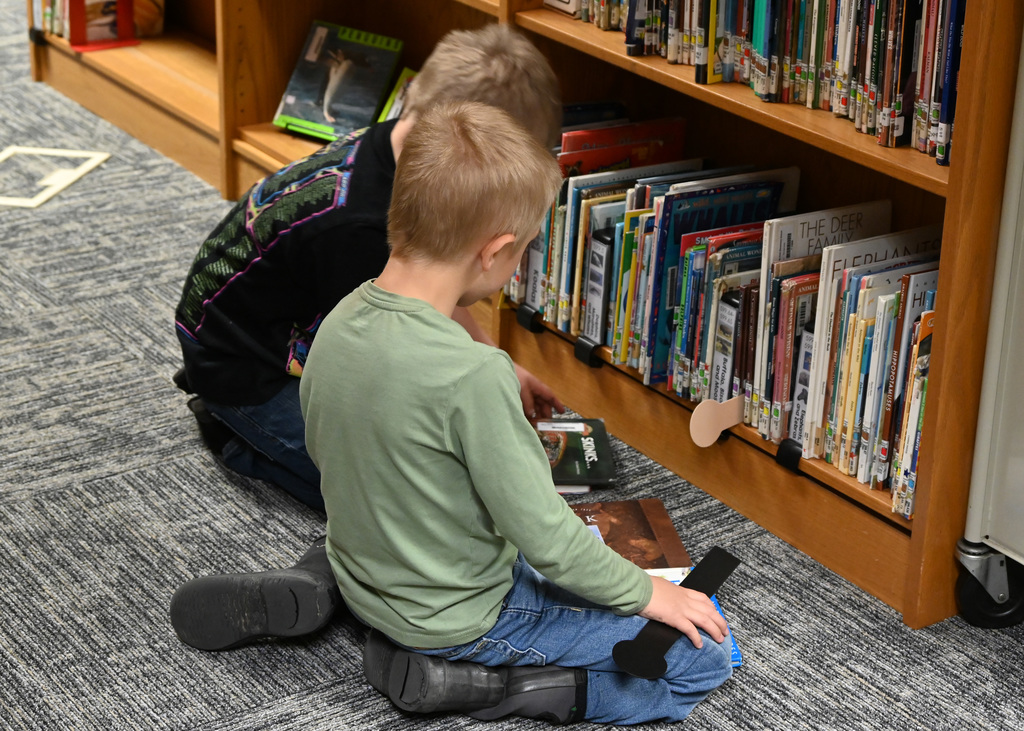 tow boys sitting on floor looking at books in front of bookshelf