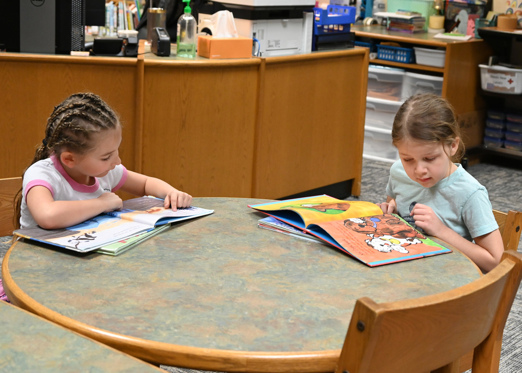 two childern sitting at a table reading books