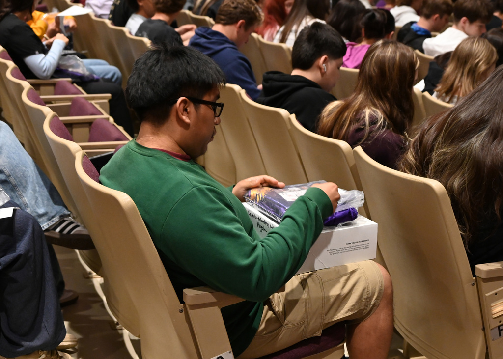 students sitting in audoitoruim. with one holding stack of packages