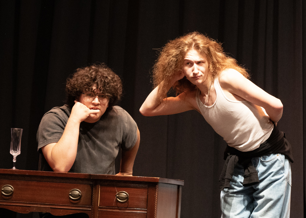 one person at desk prentending on a phone call another person hand on ear listening