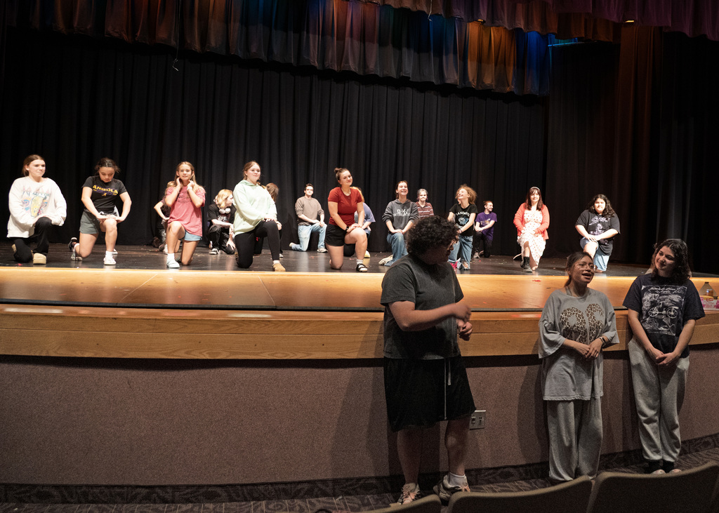 three people in front of stage with many other people on stage behind then on their knees