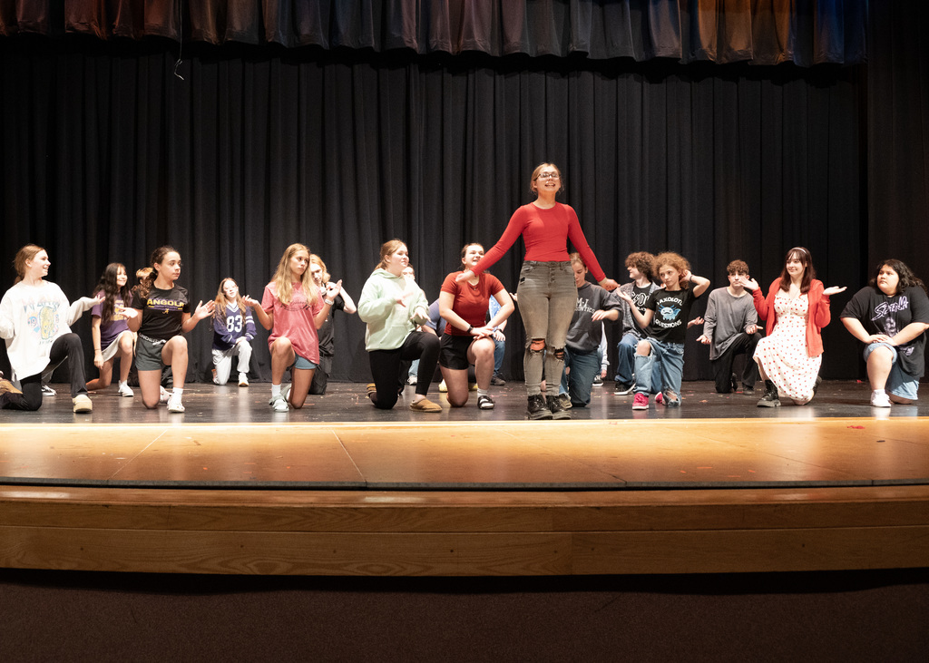 girl standing in fron of group on thier knees on a stage