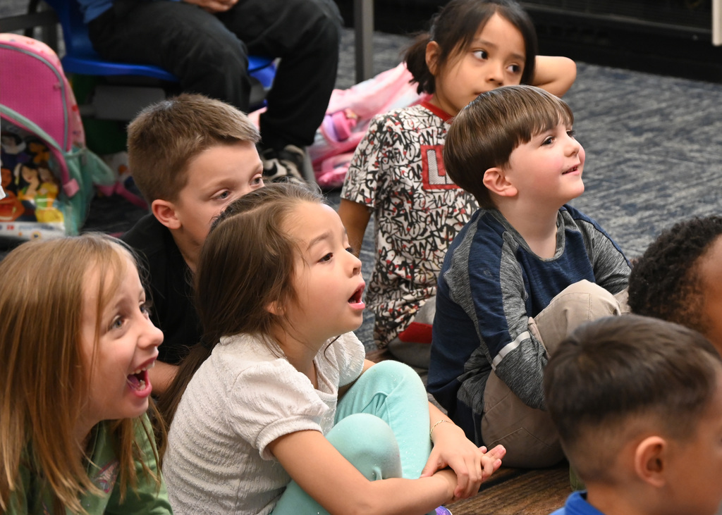 Childern sitting on floor listening reactine in smiles and surprise