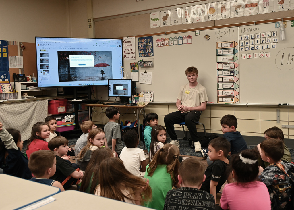 Childern sitting on floor listening to story by person sitting in chair in front of room