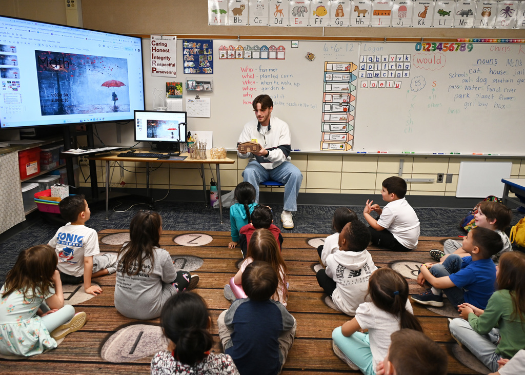 children sitting on floor listening to story being told by person in front of room