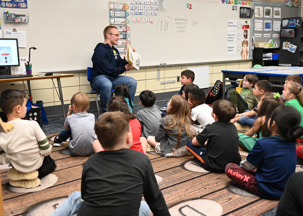 students sitting on floor listening as person in front shows book