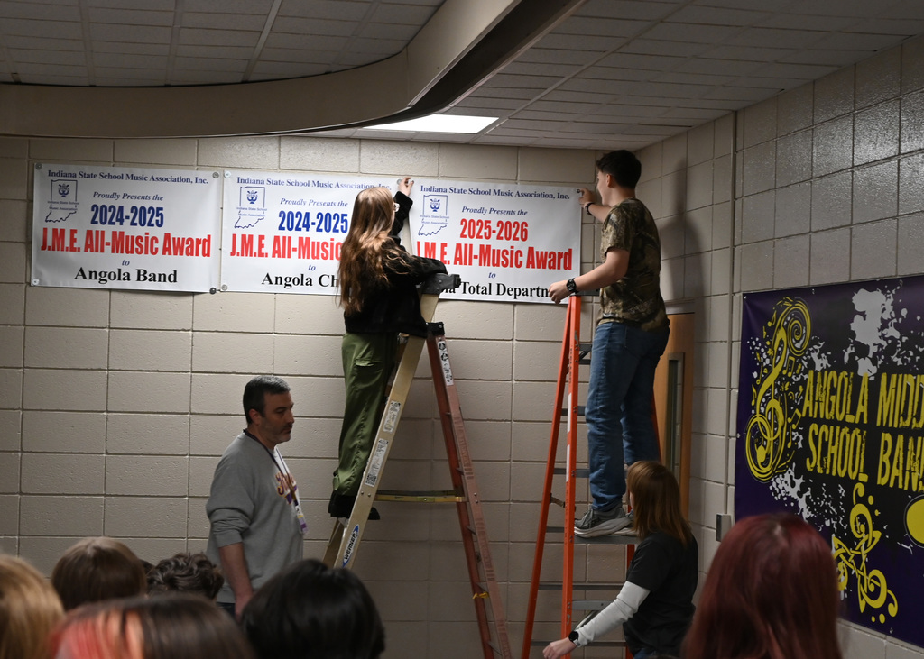 Two people on ladders hanging up a banner while other look on