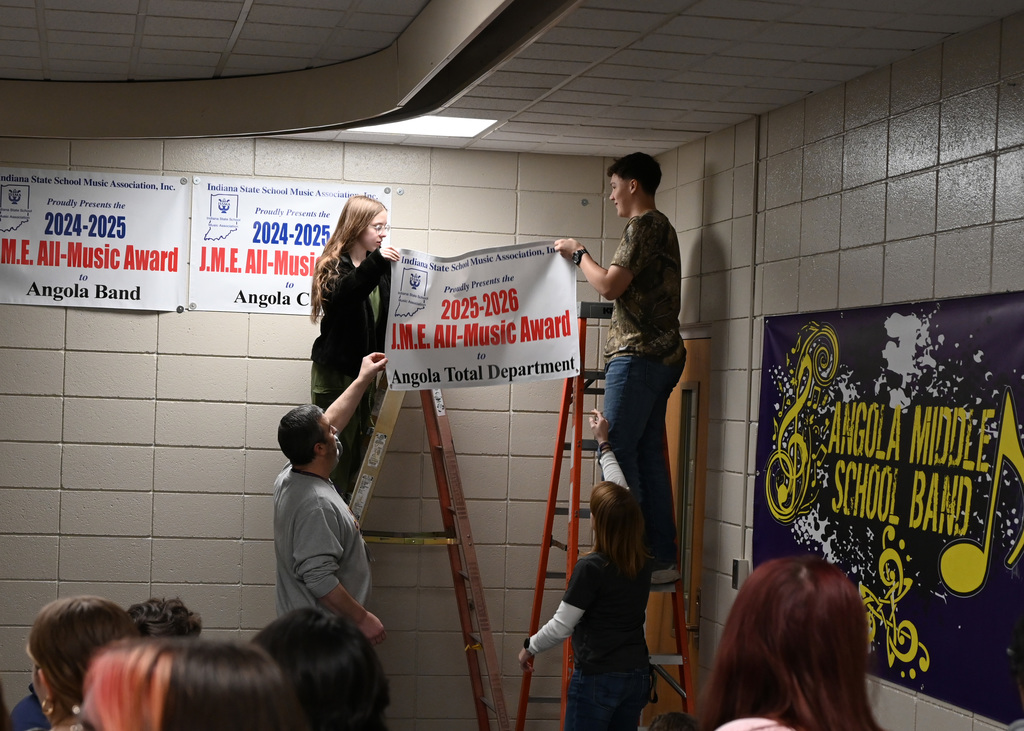 Two people on ladders being handed a banner by two othe people to hang up while other look on