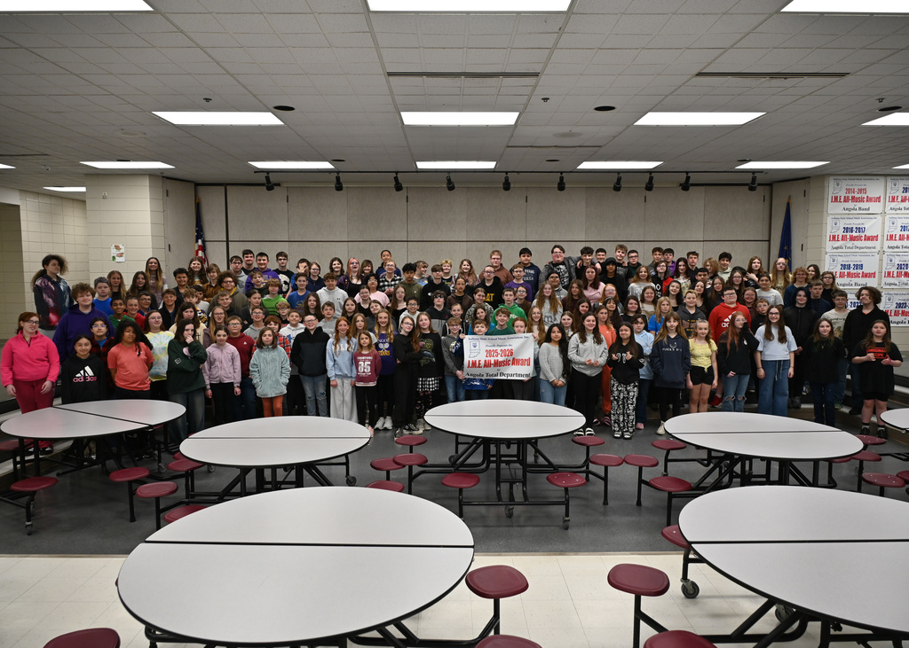 very large group of students posing for picture in a cafeteria students in front are holding up a bannder