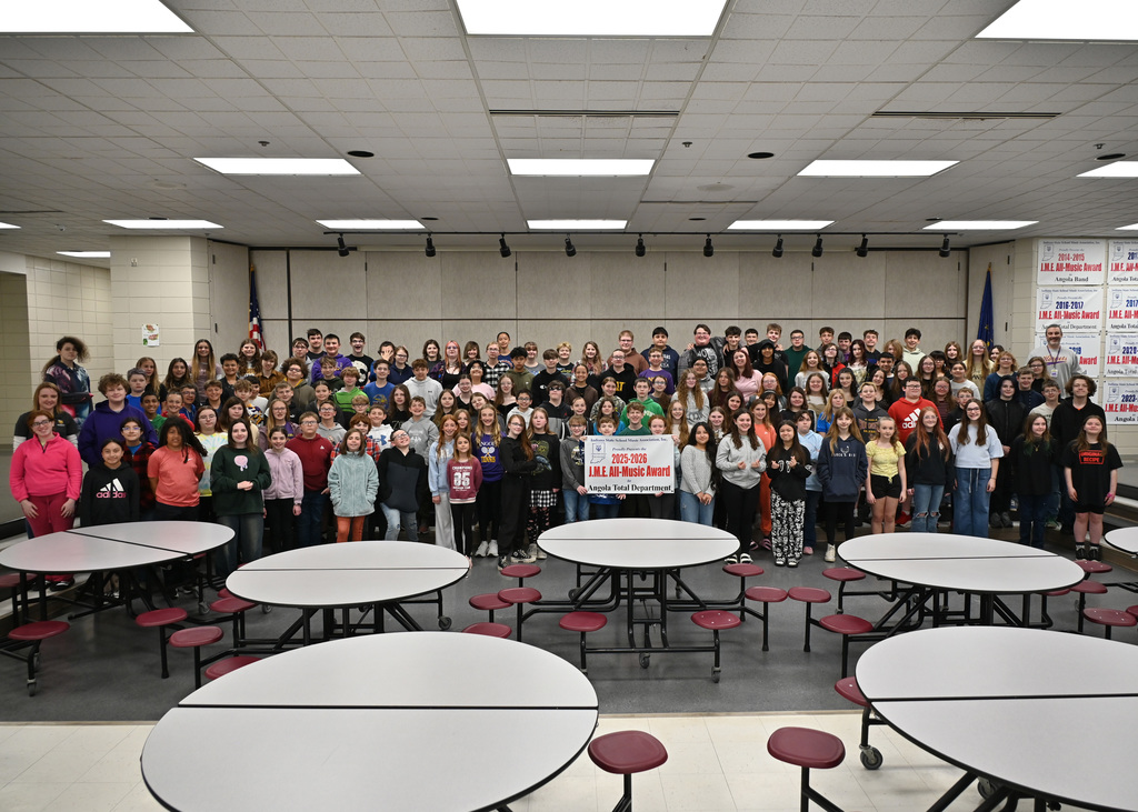 very large group of students posing for picture in a cafeteria students in front are holding up a bannder