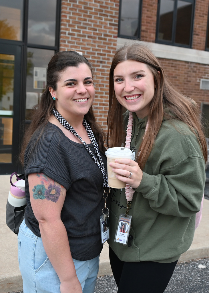 two women standing side by side smiling holding coffee