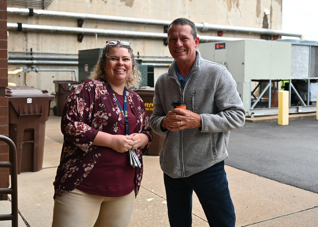 two people standing together smiling, one holding coffee