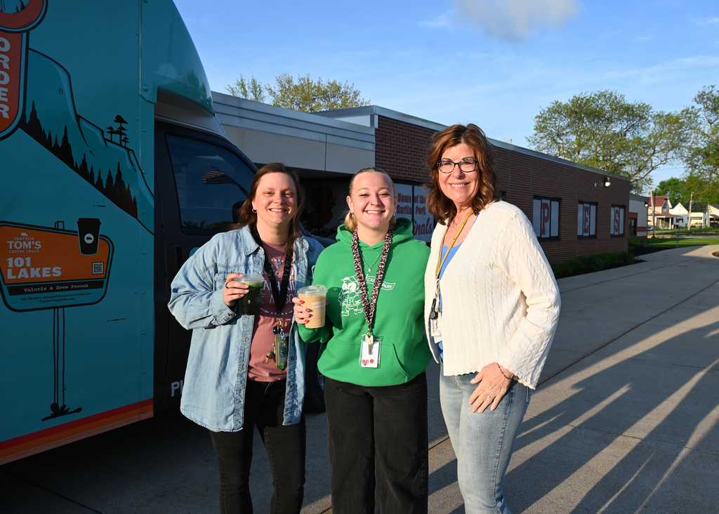 Three women standing together holding coffee, smiling