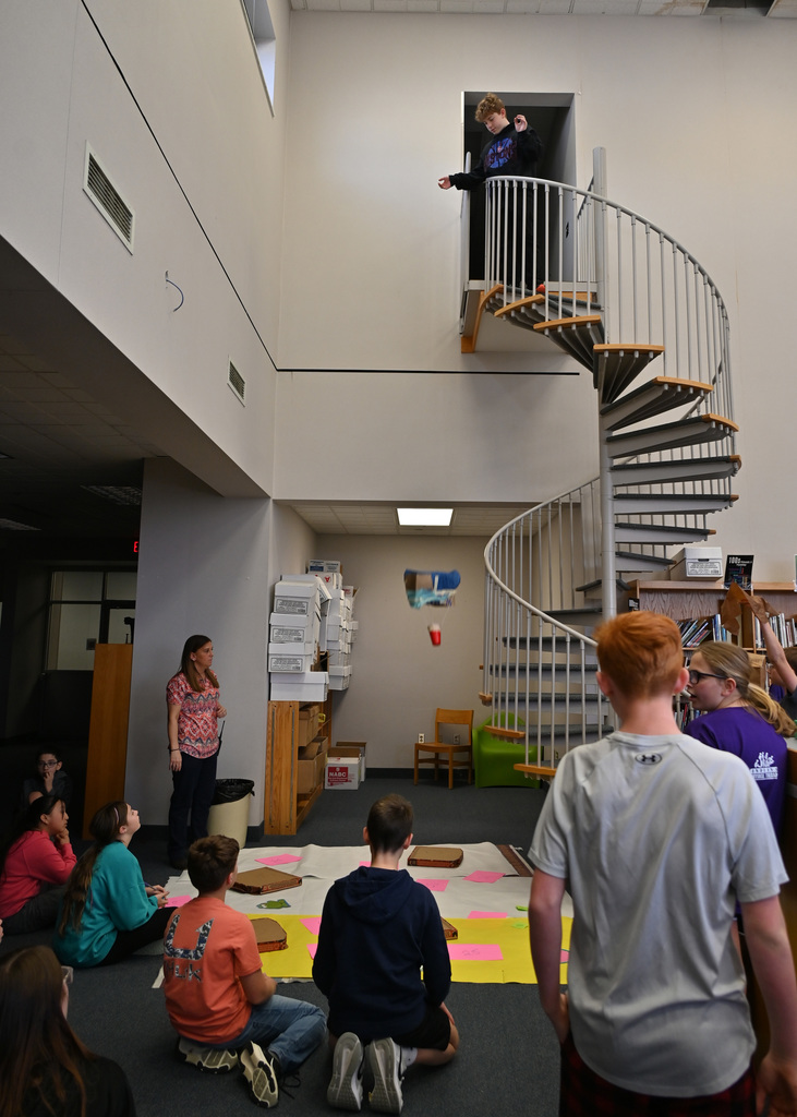 class room watching as a student drops a hand make parachute from top of flight of stairs