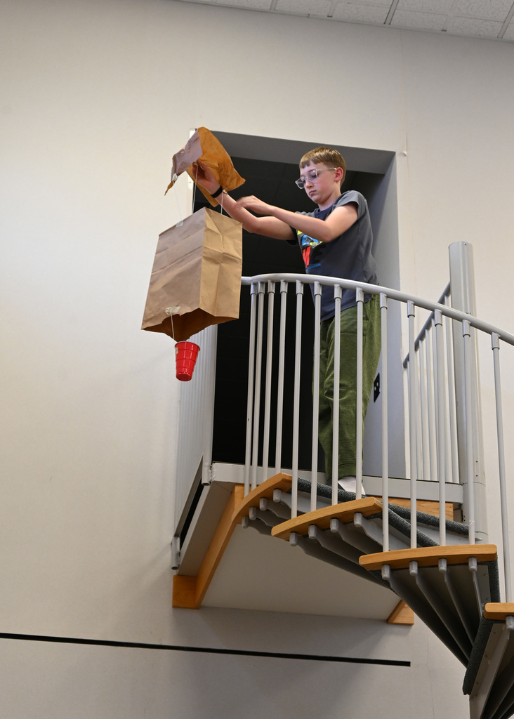 middle schooler holding a self made parachute getting ready to drop it over railing