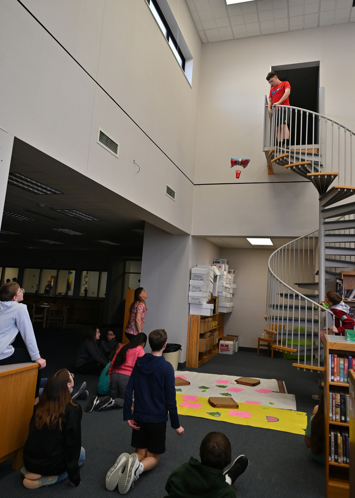 class room watching as a student drops a hand make parachute from top of flight of stairs